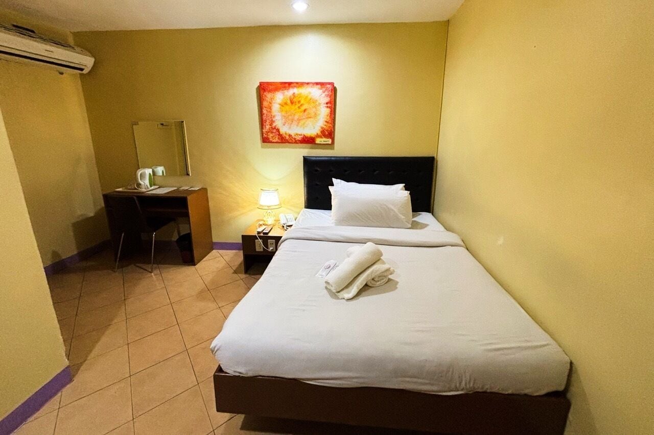 Een hotelkamer met een bed, een bureau, een stoel, een lamp en een wandairconditioner.