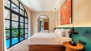 A modern hotel room with a large bed, a wooden bedside table, a view of a swimming pool, and a large window with curtains. - La Jolla Canggu (Canggu)
