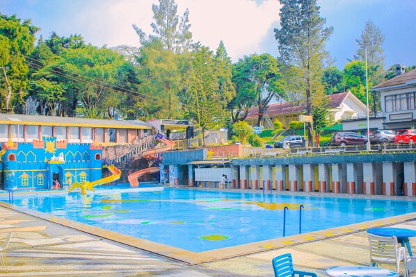 Una piscina con un tobogán con temática de castillo, rodeada de árboles y edificios.