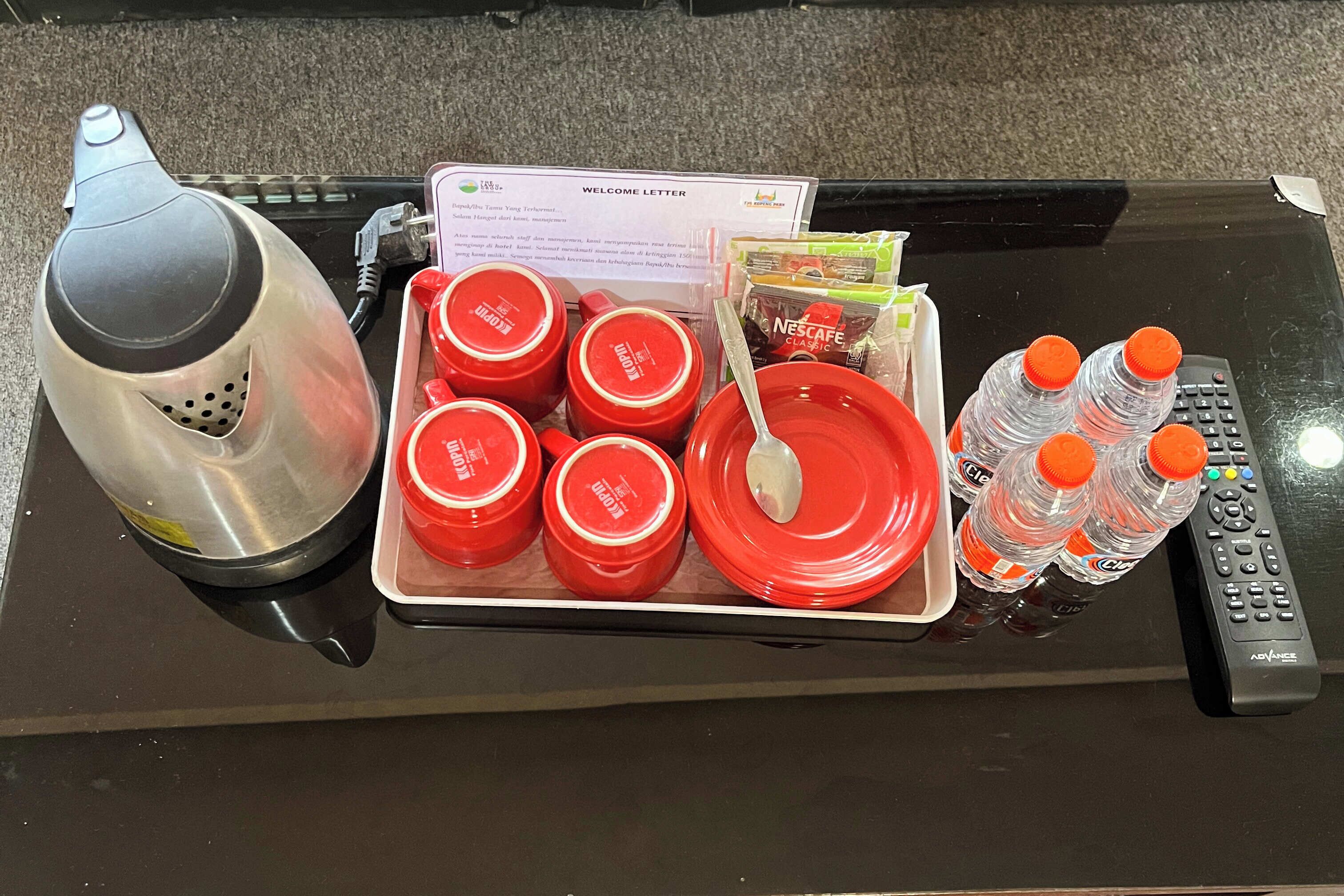 A tray with red cups, a Nescafe Classic sachet, a spoon, and water bottles on a table.