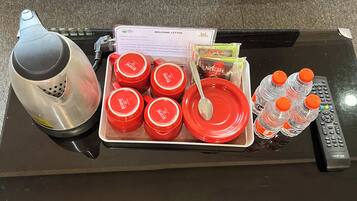 A tray with red cups, a Nescafe Classic sachet, a spoon, and water bottles on a table.