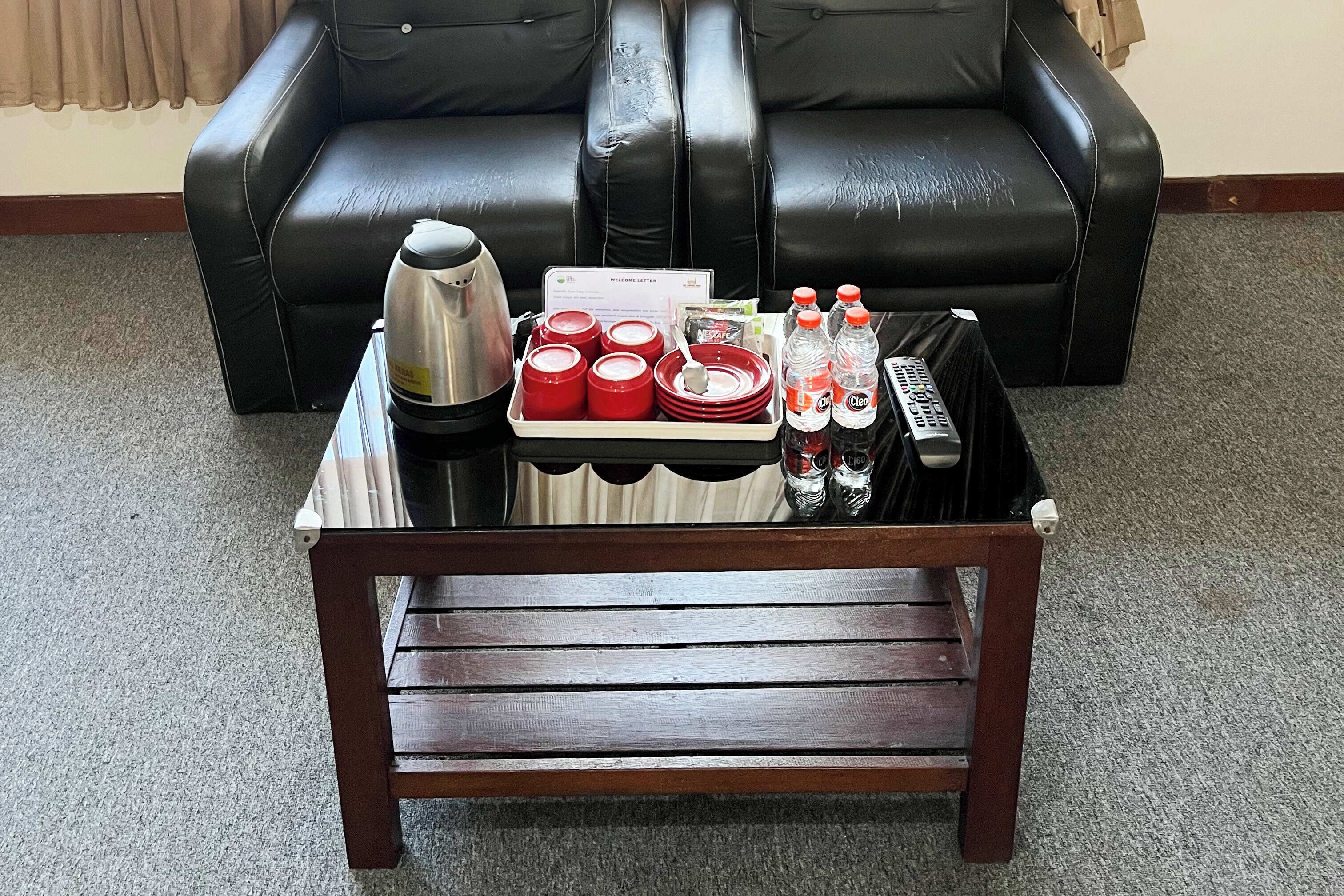 A small wooden table with a tray containing red cups, a silver pot, and a remote control.