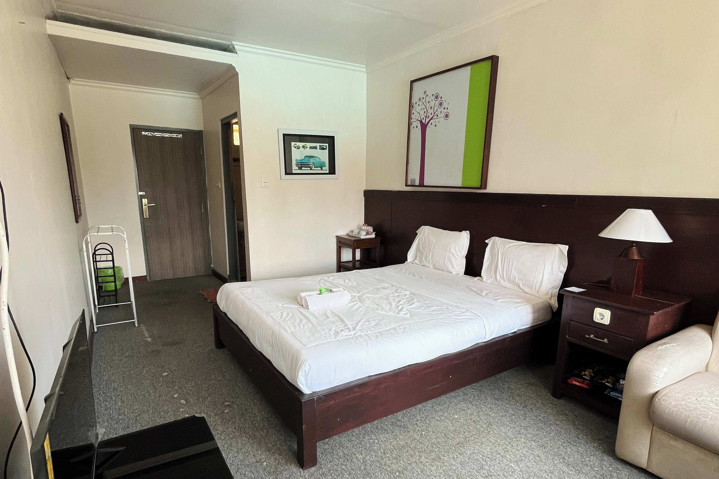 Habitación de hotel con cama, mesita de noche, lámpara, silla y un cuadro en la pared.