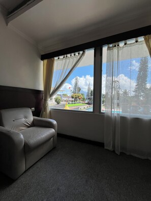 A room with a single leather sofa, a large window with sheer curtains, and a view of a train station and greenery. - Kopeng Highland Resort (Getasan)
