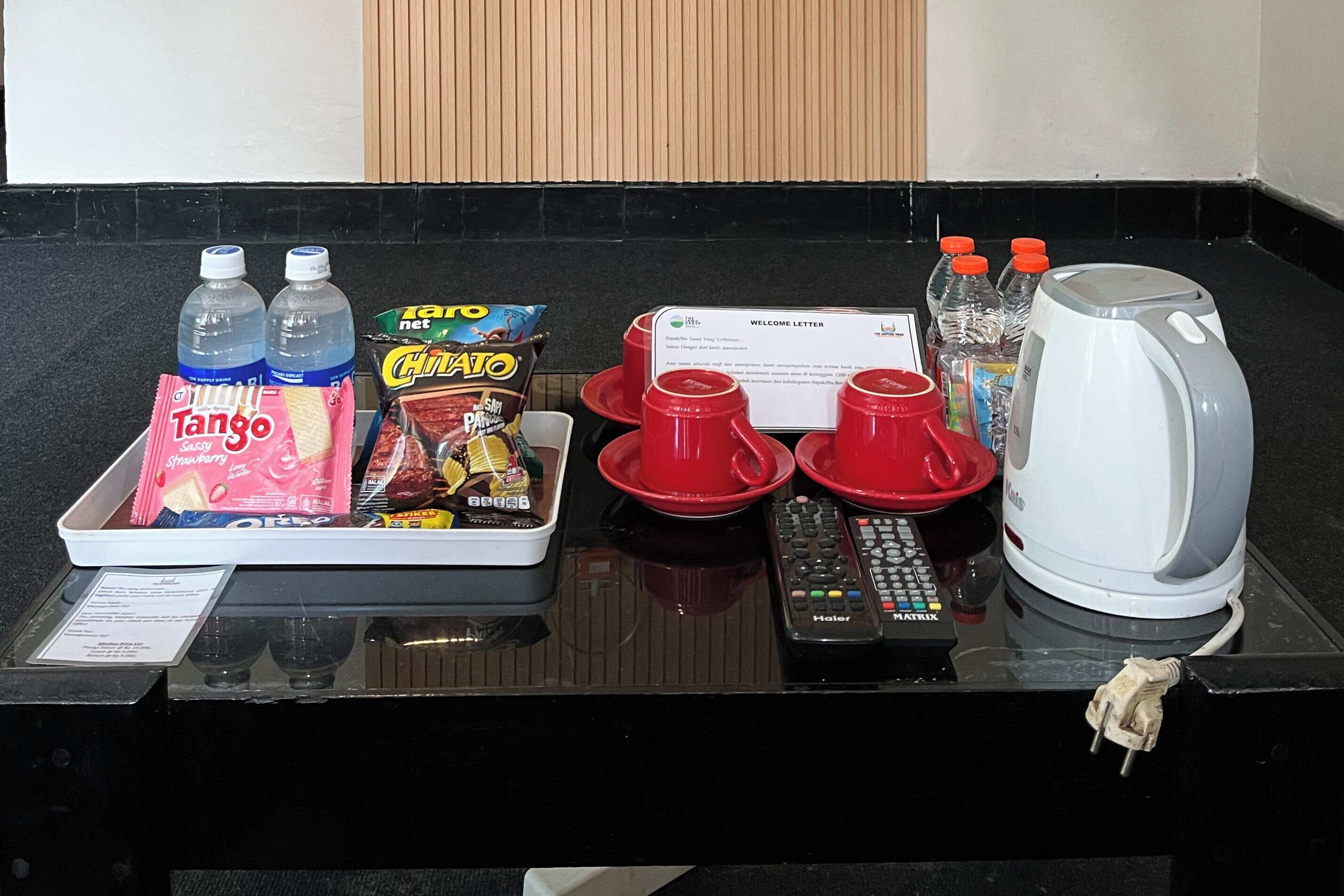 Een hotel receptiebalie met een welkomstbrief, twee waterflessen, een pak Tango, een pak Chia, en een groot aantal bakjes aardbeien.