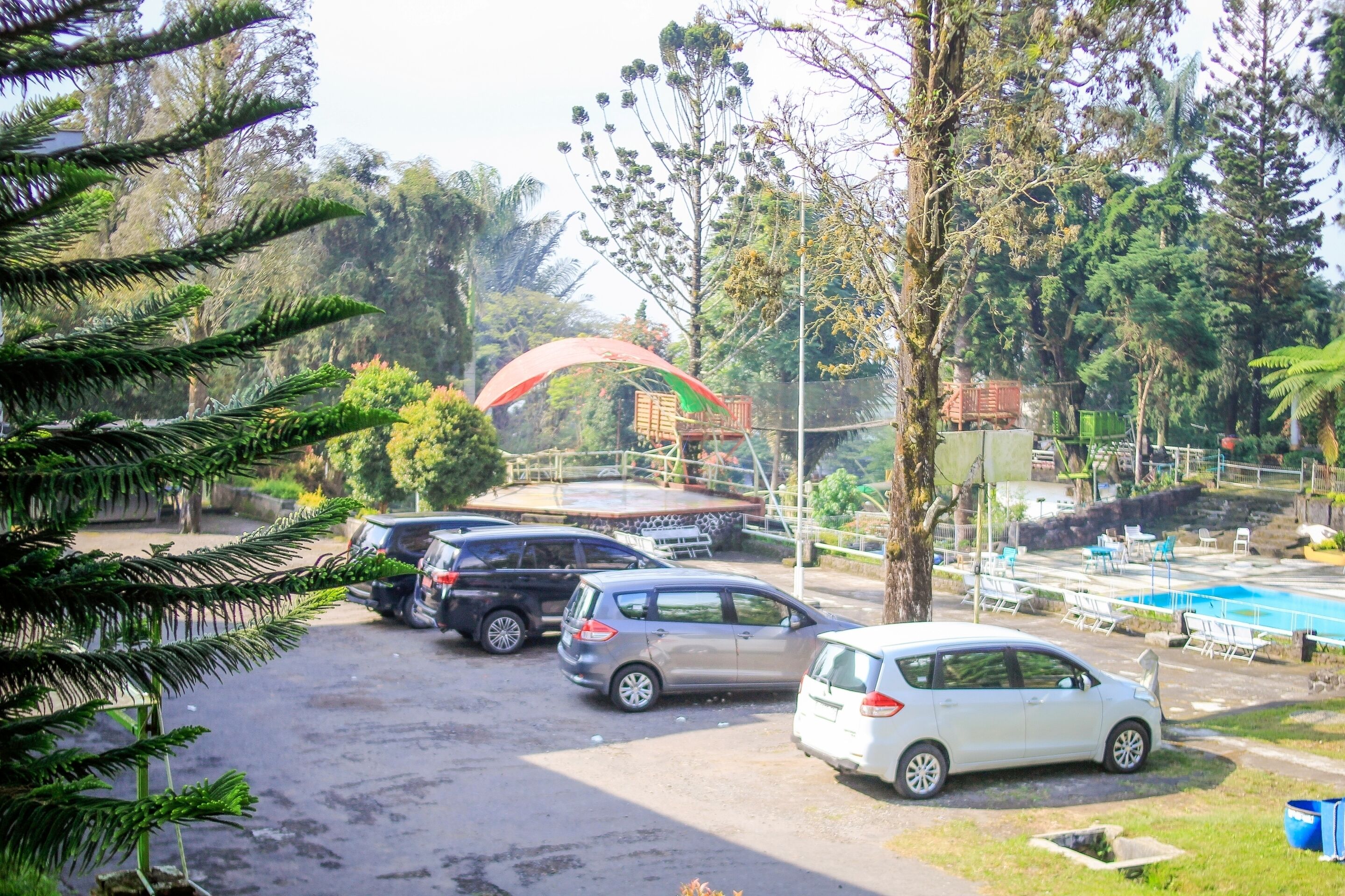 A parking area with several cars, a red canopy structure, and a swimming pool in the background.