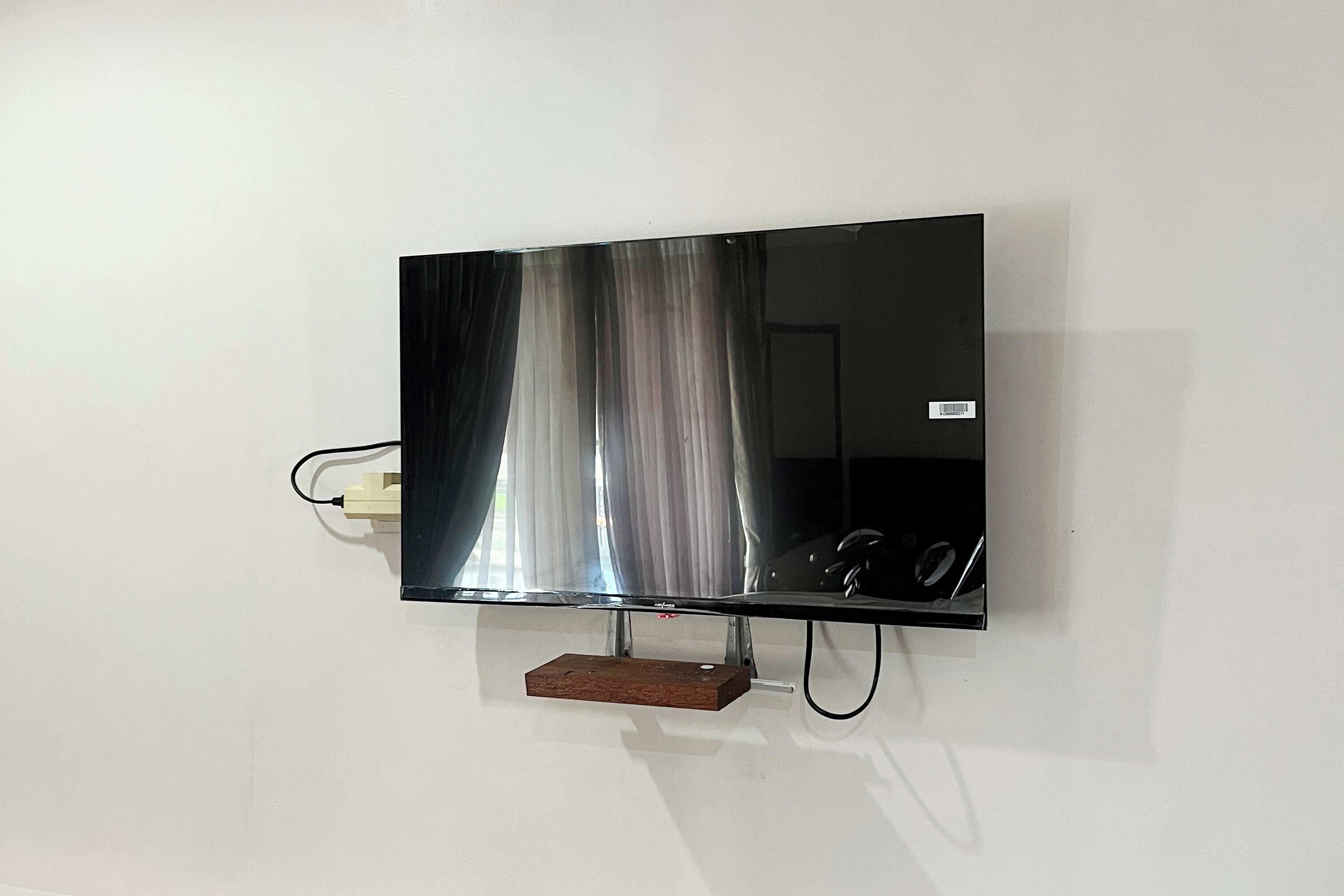 A flat-screen TV mounted on a wall with a wooden shelf below it.