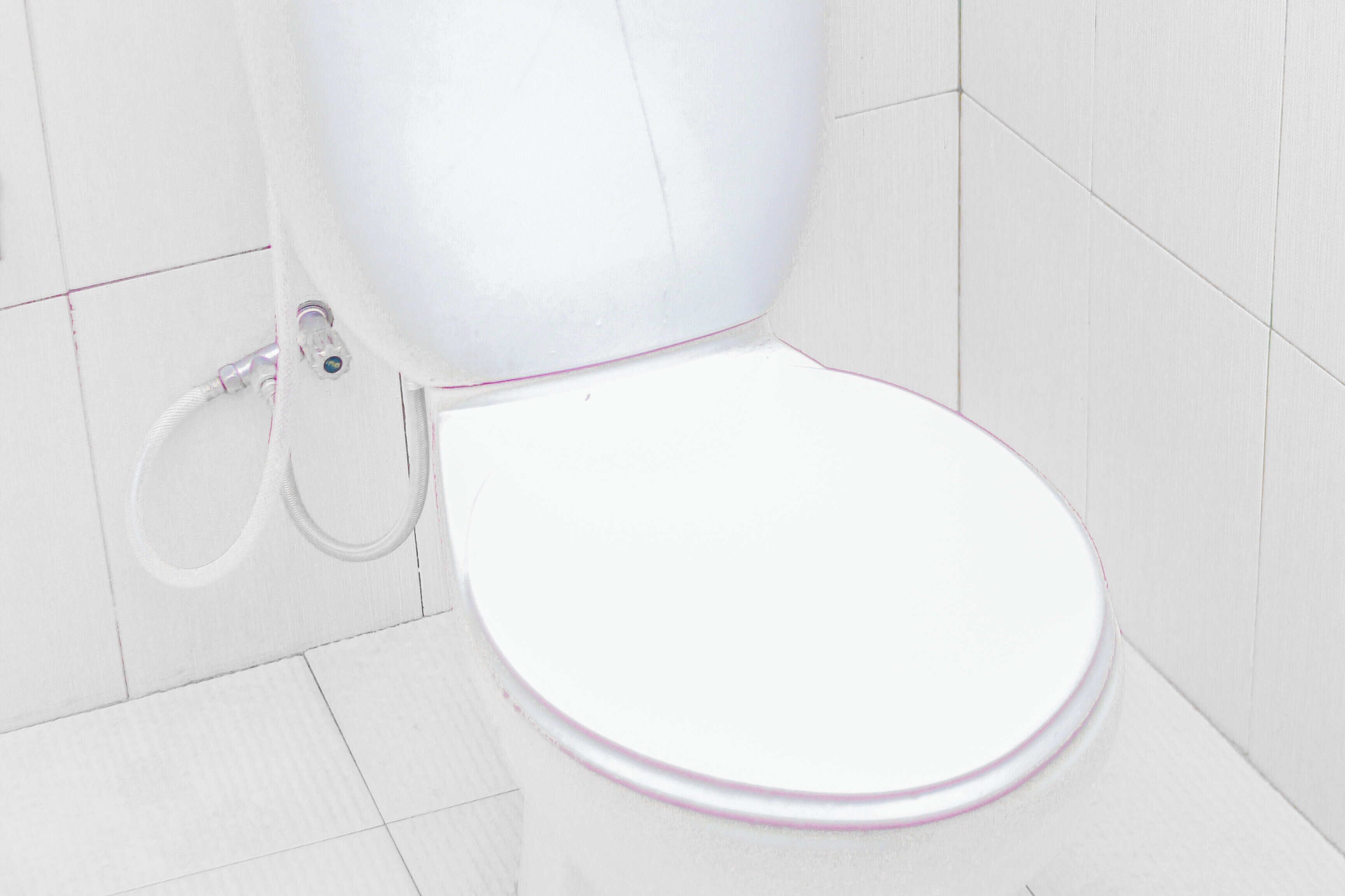 A white toilet with a pink rim, a visible flush handle, and a visible flush pipe.