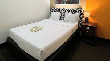 A neatly made bed with white linens, a bedside table with a lamp, and a patterned headboard.