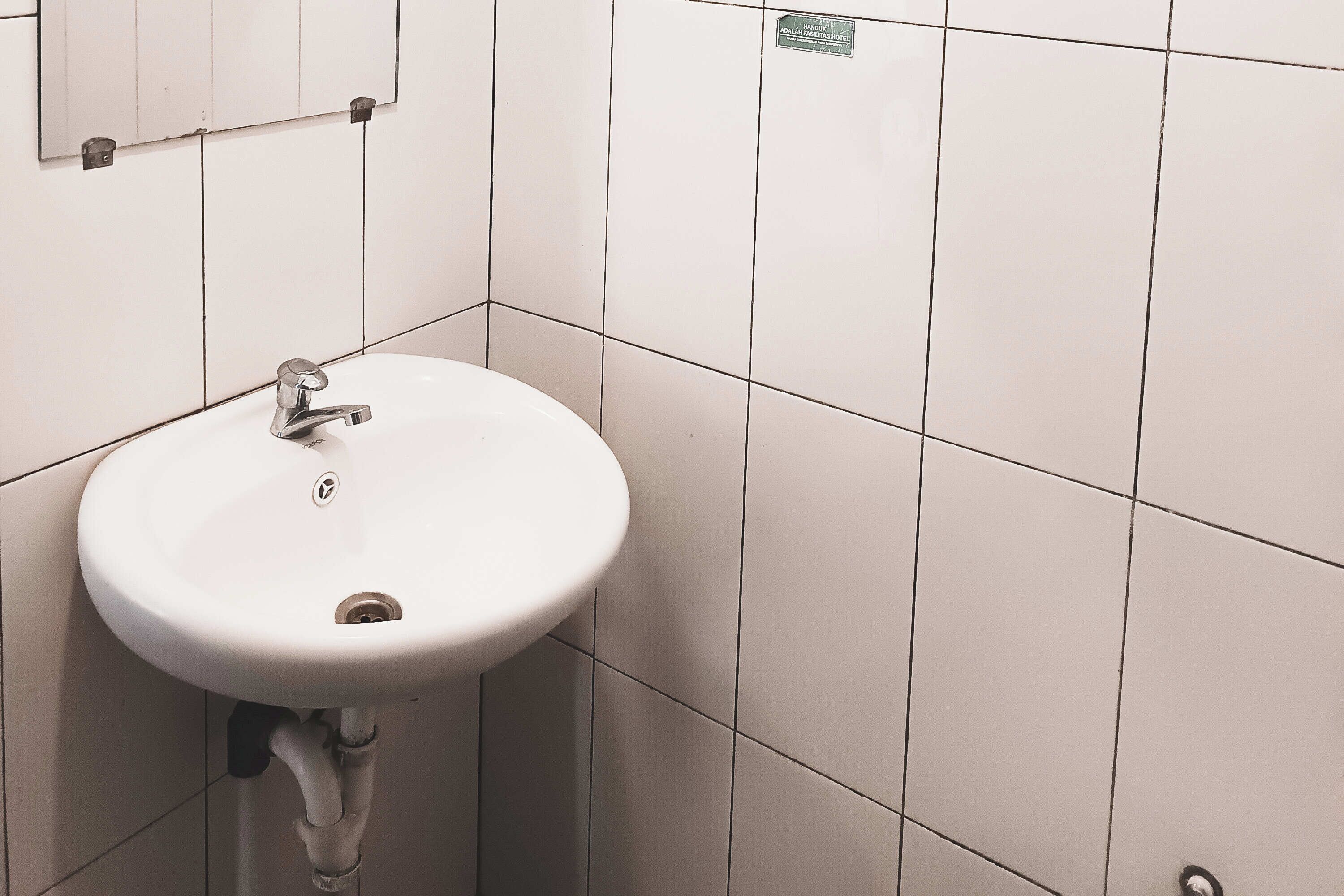 A white bathroom sink with a chrome faucet, mounted on a tiled wall.
