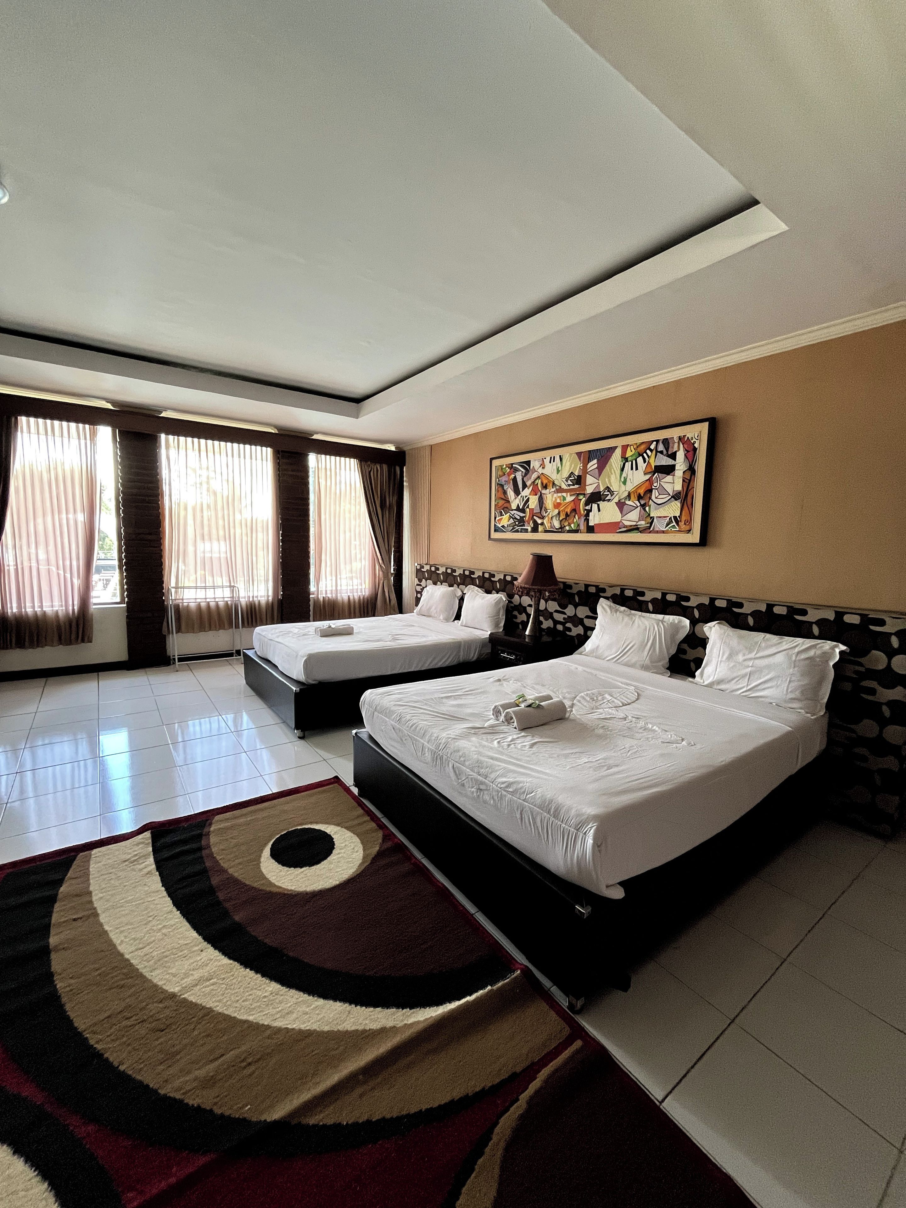 A hotel room with two beds, a large abstract painting, and a patterned rug.
