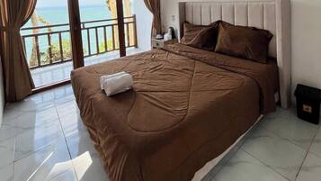 A bedroom with a large bed, a nightstand, and a view of the sea.