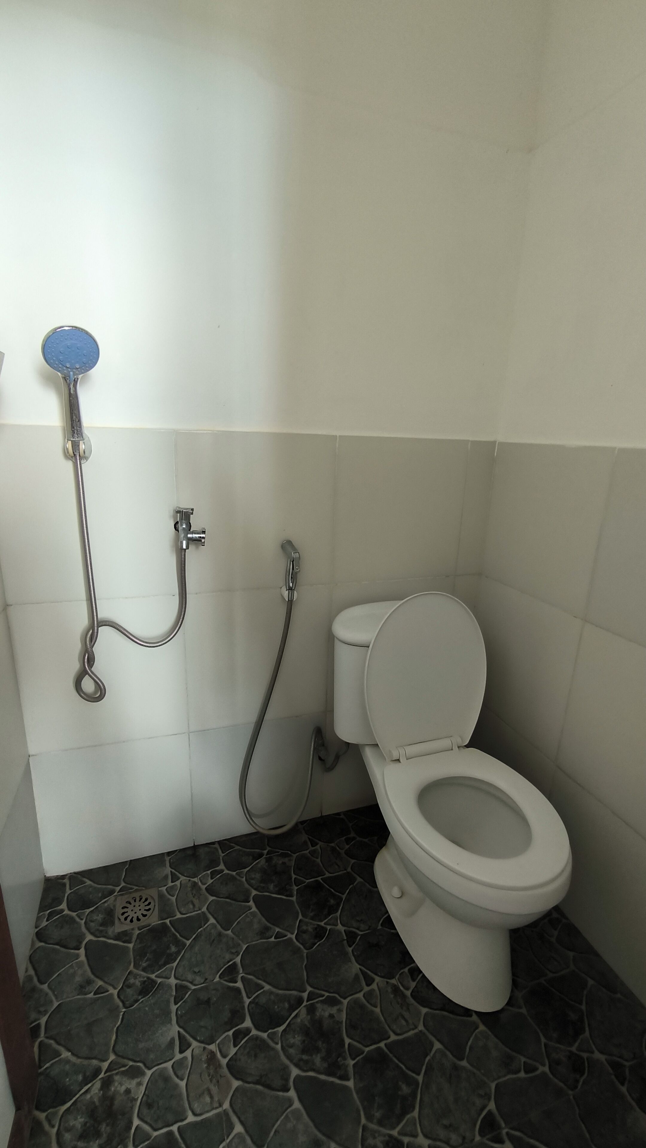 Un baño con inodoro, ducha y piso con diseño de piedra.
