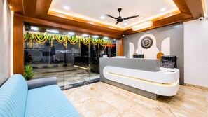 A hotel reception area with a reception desk, a ceiling fan, and a glass wall providing a view of the street. - Matrushree Hotels - Near Shree Dwarkadhish Temple (Dwarka)