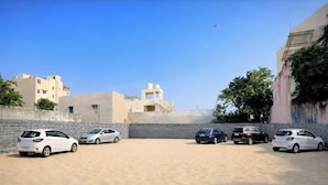 A parking area with five cars parked in a row, a clear sky, and buildings in the background. - Matrushree Hotels - Near Shree Dwarkadhish Temple (Dwarka)