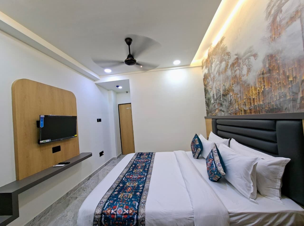 Habitación de hotel con una cama, un televisor montado en un panel de madera, un ventilador de techo y un cuadro grande en la pared.