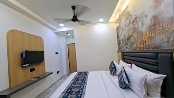 Habitación de hotel con una cama, un televisor montado en un panel de madera, un ventilador de techo y un cuadro grande en la pared.