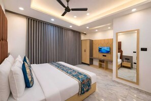 A modern hotel room with a large bed, a TV, a wardrobe, and a mirror. - Matrushree Hotels - Near Shree Dwarkadhish Temple (Dwarka)