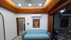 A room with a blue sofa, a framed picture on the wall, and an air conditioning unit. - Matrushree Hotels - Near Shree Dwarkadhish Temple (Dwarka)