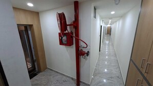 A hallway with a fire hose reel mounted on the wall, a fire alarm box, and a camera on the ceiling. - Matrushree Hotels - Near Shree Dwarkadhish Temple (Dwarka)