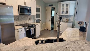 A kitchen with white cabinets, a stainless steel refrigerator, a microwave, an oven, and a sink with a stainless steel faucet.