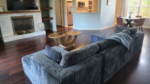 Una sala de estar con chimenea, televisor, comedor con mesa y sillas, y una cocina al fondo.