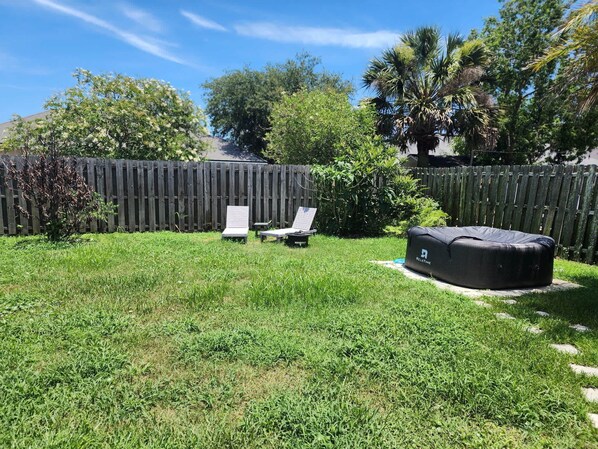 A backyard with a wooden fence, two lounge chairs, and a hot tub.