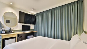 A hotel room with a bed, a desk with a computer, a flat-screen TV, a mirror, and a window with curtains. - NO25 HOTEL BUPYEONG (Incheon)