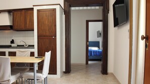 Una cocina compacta con armarios de madera, una mesa de comedor con sillas y vistas a un dormitorio con cama y televisor.