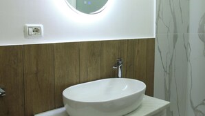 Un baño con un espejo redondo, un lavabo blanco, paneles de madera y azulejos de mármol.