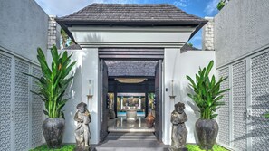 A covered entrance with a white wall, two statues, and a pathway leading to a building. - Des Indes II by Elite Havens (Kabupaten Badung)
