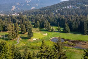A golf course with a pond, surrounded by dense forest and residential buildings in the background. - Mountain living, over 1400 sqft condo in Blueberry Hills, exceptional outdoor space, book for Summer (Whistler)