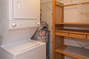A laundry area with a washing machine, a dryer, and a water heater. There are wooden shelves and a metal rack for hanging items. - Mountain living, over 1400 sqft condo in Blueberry Hills, exceptional outdoor space, book for Summer (Whistler)