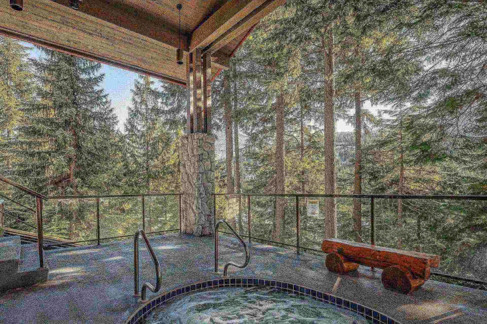 A wooden deck with a metal railing, surrounded by trees.