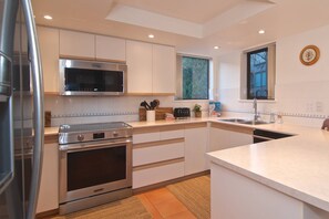 A modern kitchen with stainless steel appliances, white cabinetry, and a large window providing natural light. - Mountain living, over 1400 sqft condo in Blueberry Hills, exceptional outdoor space, book for Summer (Whistler)