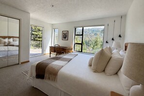A bedroom with a large bed, a desk, and a view of a forest through the windows. - Mountain living, over 1400 sqft condo in Blueberry Hills, exceptional outdoor space, book for Summer (Whistler)