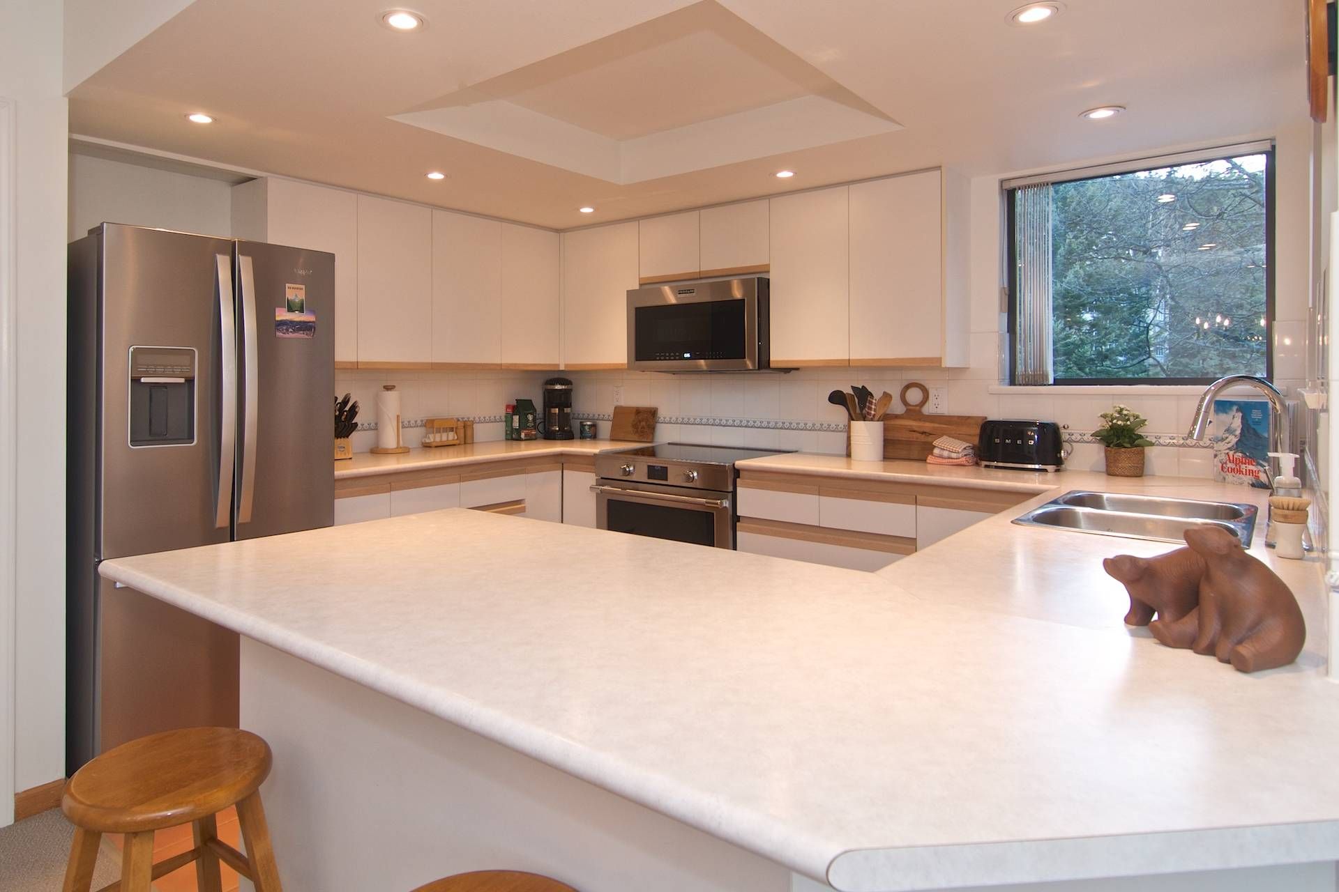 A modern kitchen with stainless steel appliances, a central island, and a window providing a view of trees.