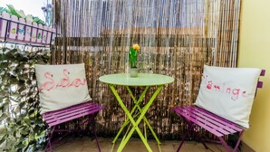 Een klein terras met een ronde tafel en twee stoelen, elk met een witte kussen met roze tekst.