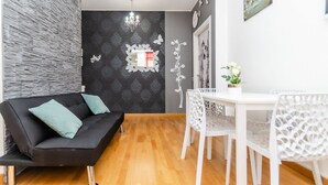 Een moderne woonkamer met een zwarte bank, witte stoelen, een bijzettafeltje en een decoratieve spiegel.