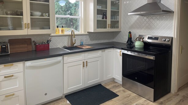 Una cucina moderna con mobili bianchi, un piano di lavoro nero, un forno in acciaio inossidabile e una finestra vista verde.
