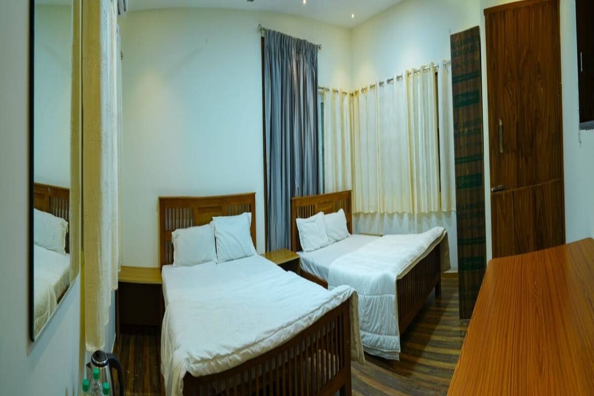 Una habitación de hotel con dos camas individuales, una mesa de madera, un espejo y una ventana con cortinas.
