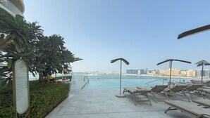 A poolside area with lounge chairs, a pool, and a view of the city skyline. - Vogue| Grand Blue Beachfront Designed By Elie Saab (Dubai)