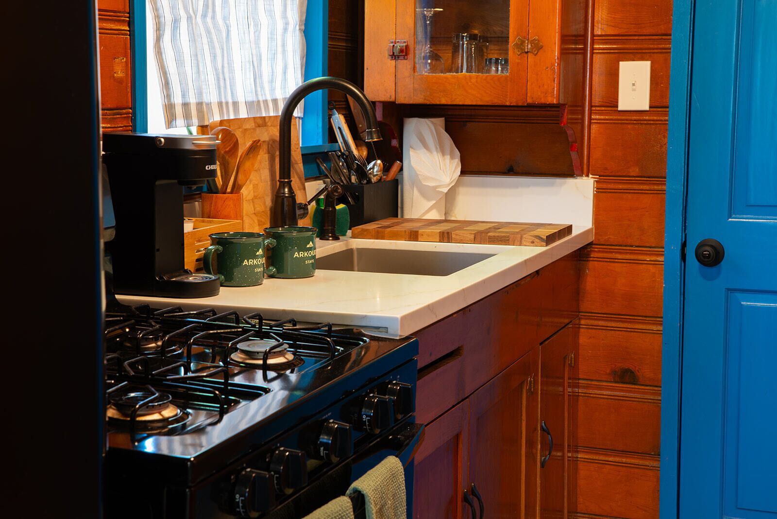 Una cocina con estufa a gas, lavamanos, armarios de madera y una puerta azul.