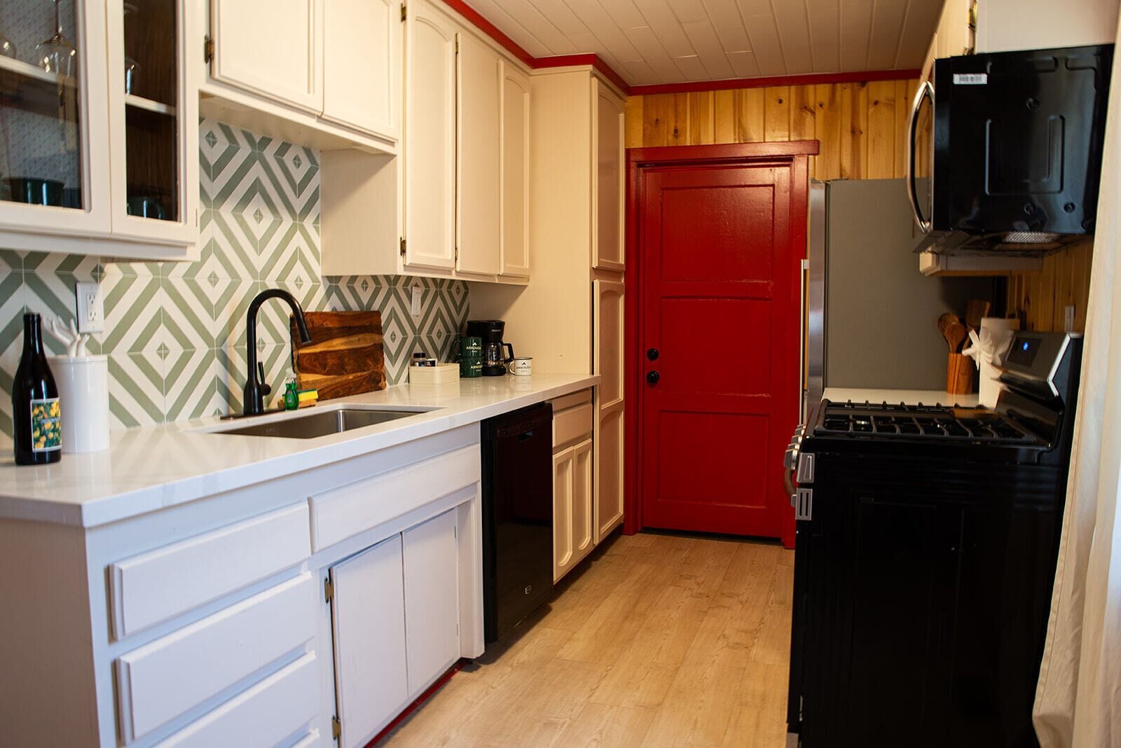 A kitchen with white cabinets, a red door, a black stove, and a microwave.
