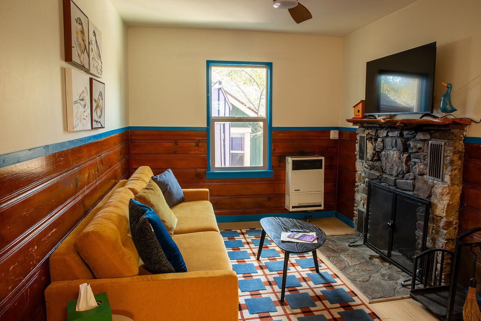 A cozy living room with a sofa, a fireplace, a television, and a window with a view of a building outside.