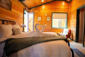 A cozy wooden room with a bed, a swan-shaped pillow, a window, and a door. - Arkouda Cabins (Big Bear Lake)
