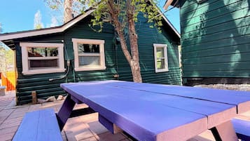 Una mesa de picnic frente a un edificio verde con ventanas y un árbol.