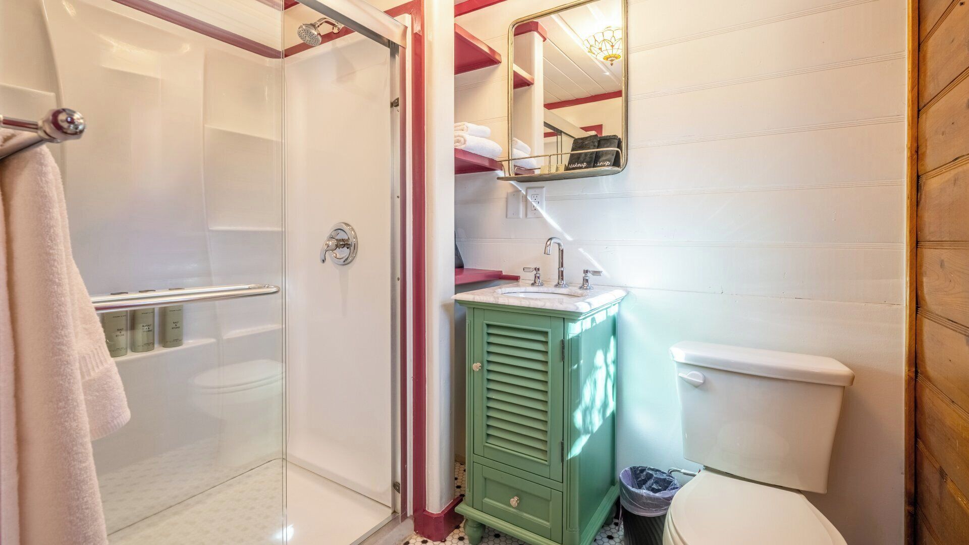 A bathroom with a glass shower enclosure, a green vanity, a white toilet, and a mirror above the sink.