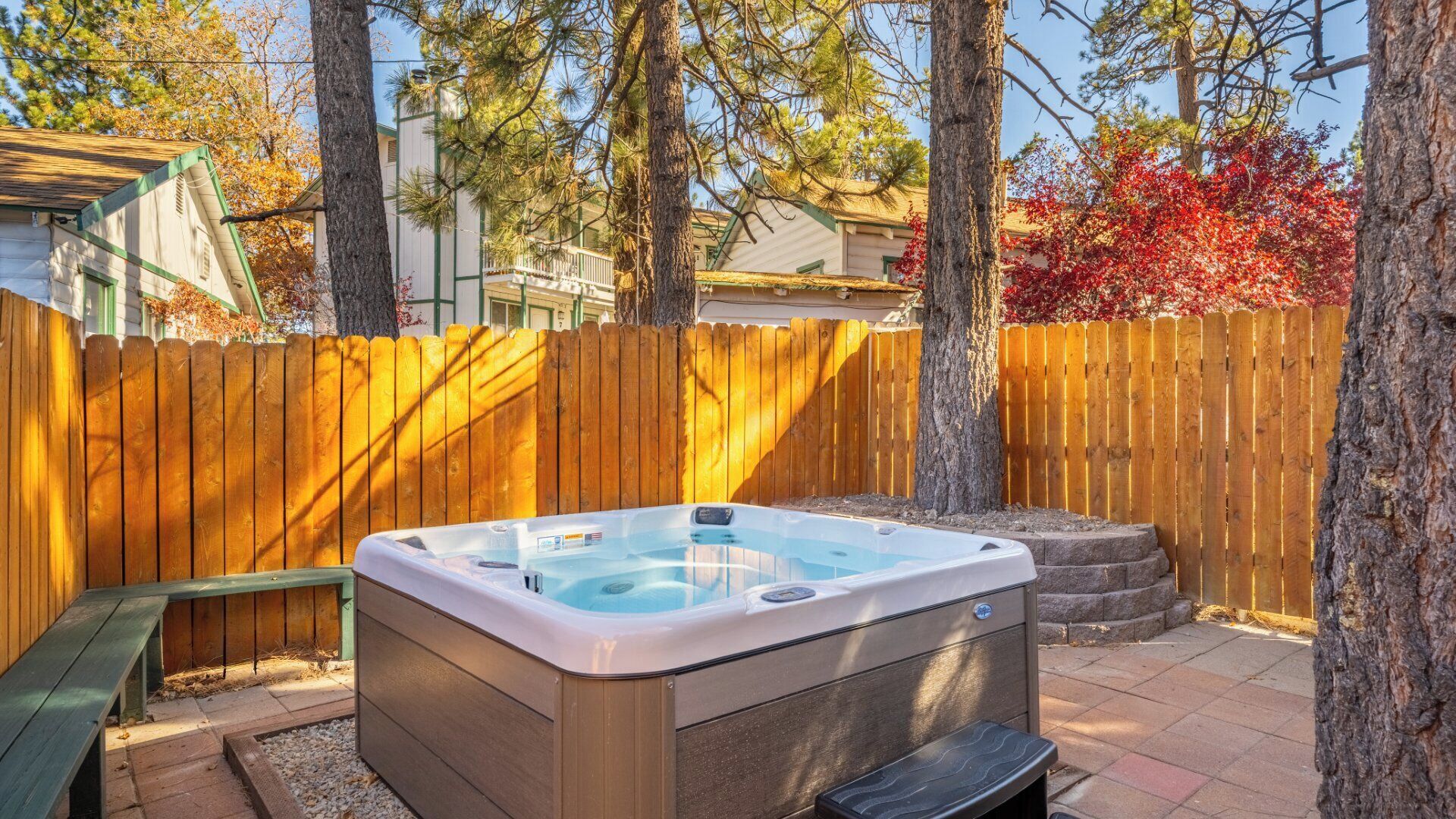 Een hottub in een achtertuin met een houten schutting, bomen en een bankje.