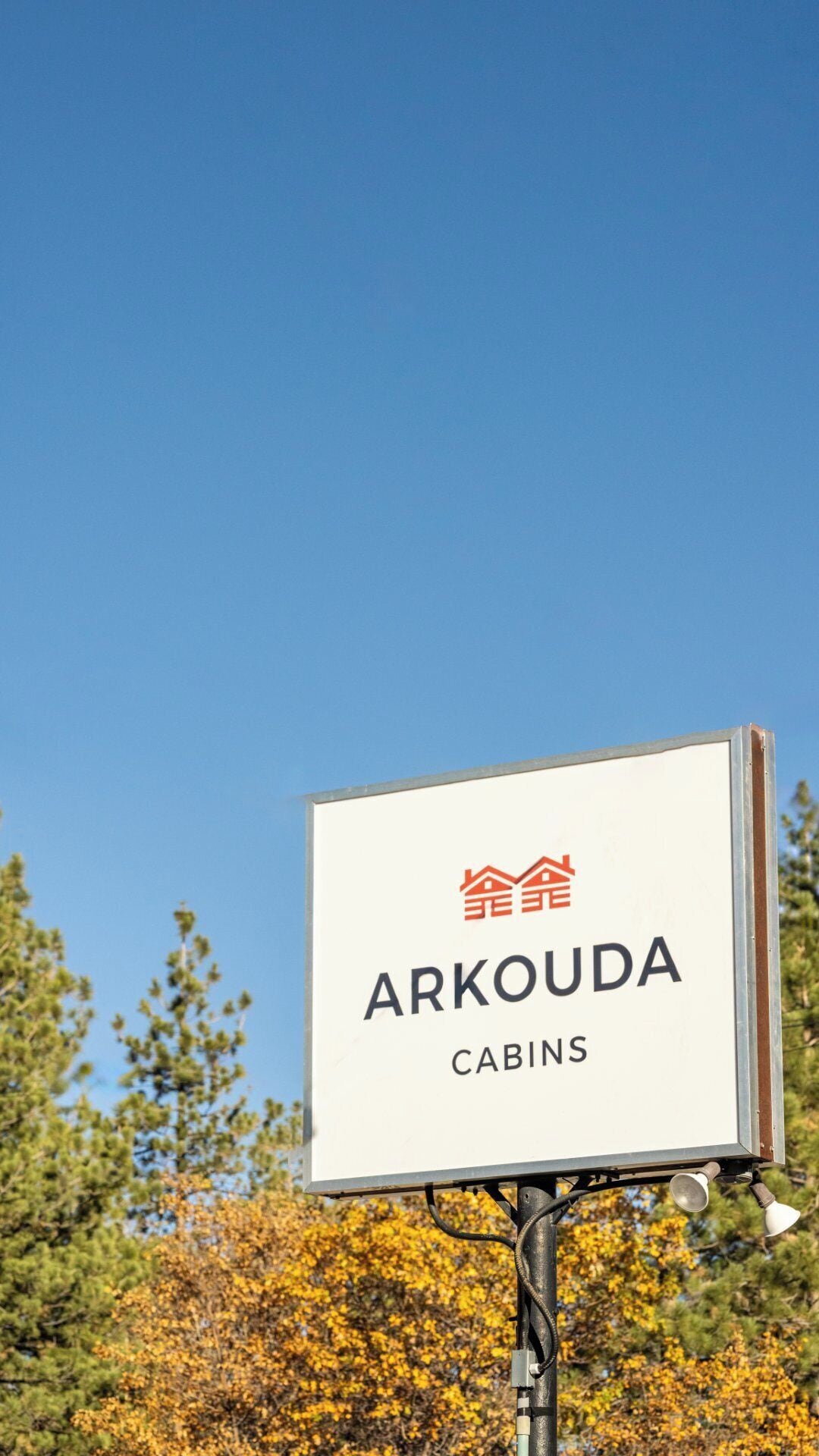 Señal de Arkouda Cabins con cielo despejado y árboles al fondo.